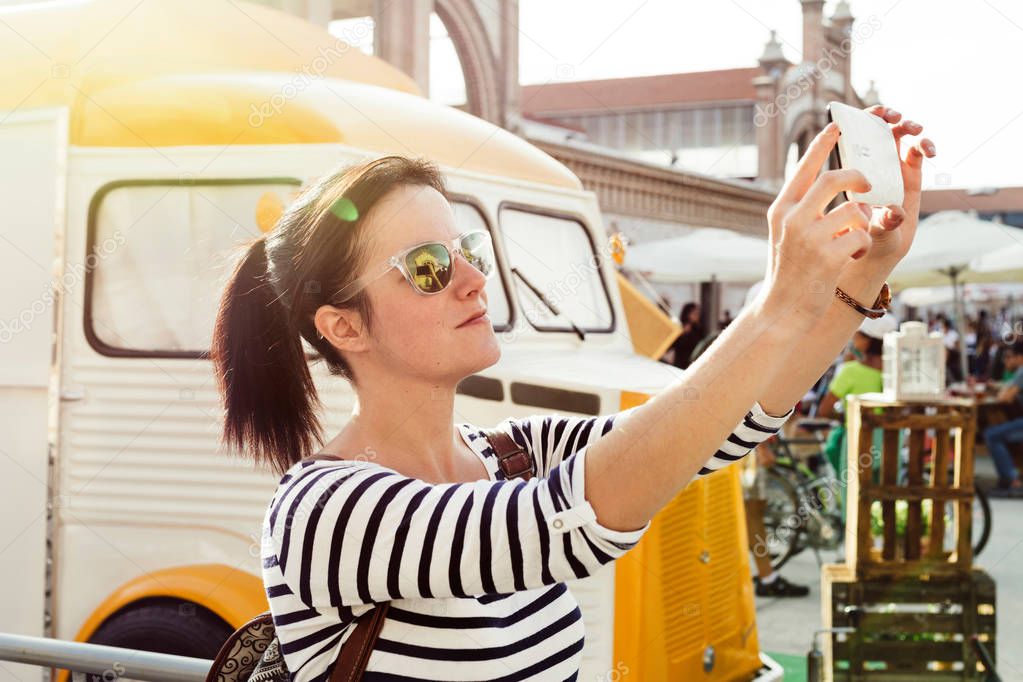 Young woman making a selfie, next to the vintage style food truck, at an outdoor even