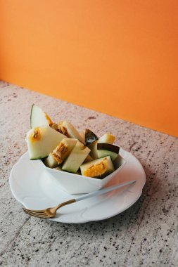 Granit tezgah ve turuncu arka plan üzerinde renkli yaz tema geometrik kase kavun kurbağa deriyi kesme