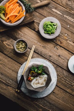 Asya şehriye çorbası geometrik kase yemek çubukları, ahşap masa ve taze sebze ile