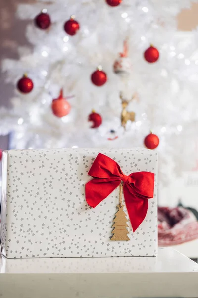 Geschenk Mit Roter Schleife Und Karte Vor Weißem Weihnachtsbaum Dekoriert — Stockfoto