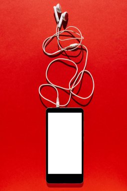 Hareket eden telefon boş ekran ve kulaklık üzerinde kırmızı arka plan ile. Kopya alanı ile üstten görünüm