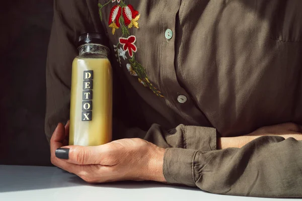 Woman in a green button-down shirt holding a bottle of green jui — Stock Photo, Image