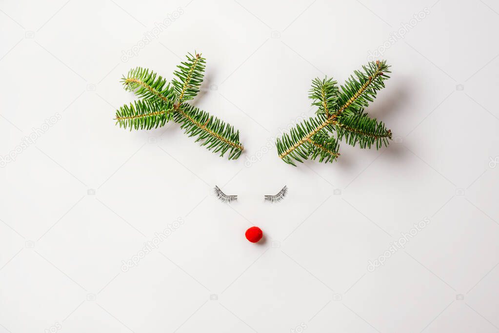 christmas reindeer concept made of evergreen fir, bauble decoration, tabs and antlers on pastel light background. Minimal winter holidays idea. Flat lay top view composition.