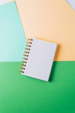 Renkli pastel arka planda altın spiral ve boş sayfalı defter..