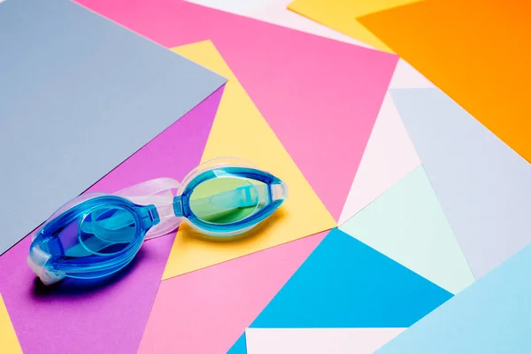 Modré plavecké brýle s gumovým popruhem na vícebarevném geometrickém pozadí. — Stock fotografie