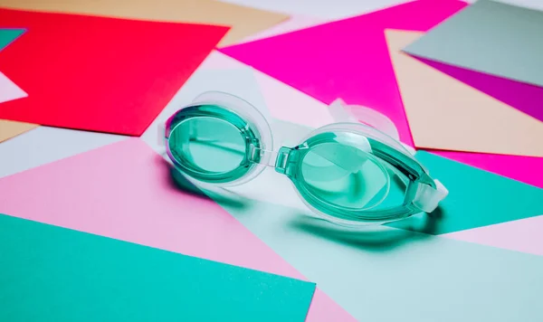 Óculos de natação turquesa, com pulseira de borracha em fundo geométrico multicolorido . — Fotografia de Stock