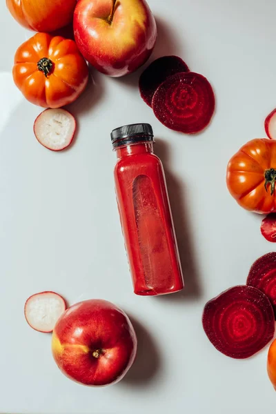 Red smoothie drink in bottle near ripe apples tomatoes and beets. Detox diet for healthy body and mind. health food concept. On light background