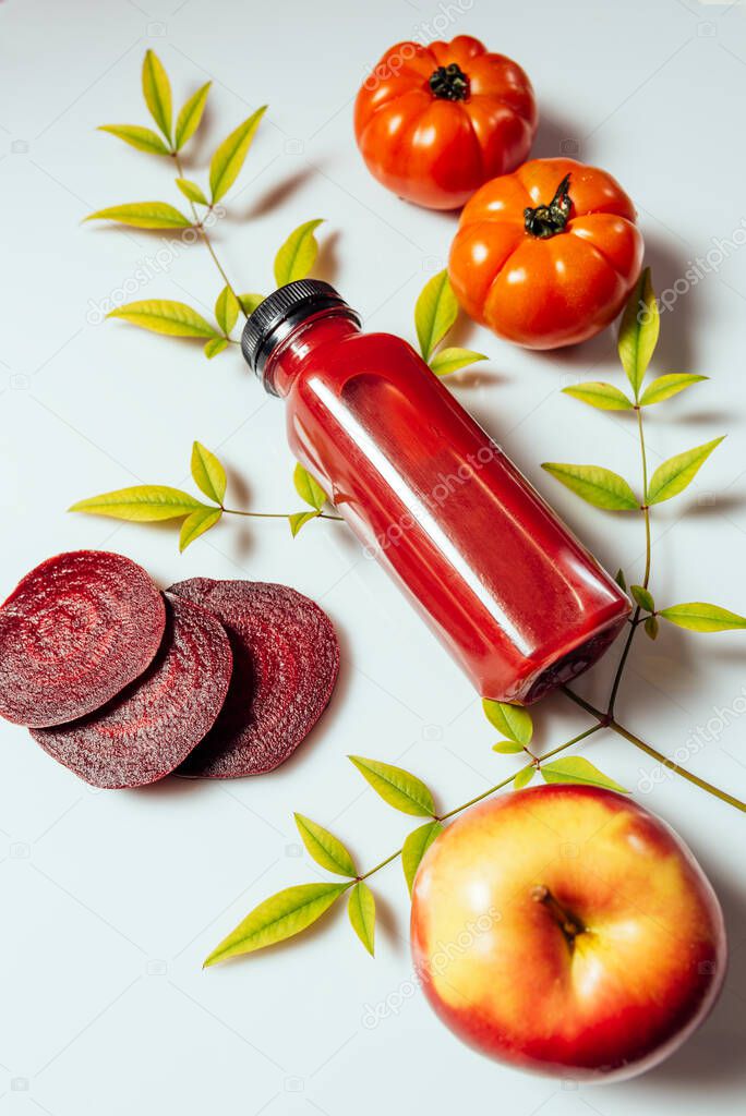 Red smoothie drink in bottle near ripe apples tomatoes and beets. Detox diet for healthy body and mind. health food concept. On light background