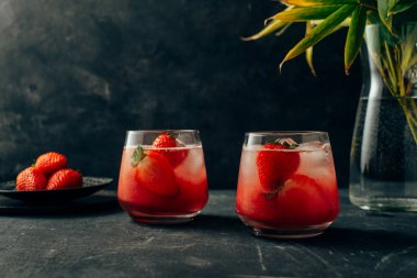 İki lezzetli çilekli kokteyl. Doğal çilek ve buz küpleriyle taze yaz kokteyli. Arkaplanda bir bardak çilekli soda var. Ön görünüm