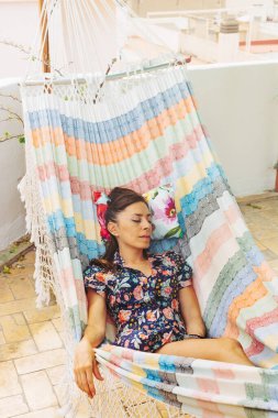 Güzel, rahat bir kadın, hamakta uyuyor, çiçekli bir elbise içinde. İspanya 'da bir yaz günü çatıda huzur verici bir tatil.