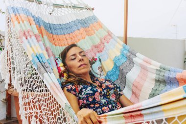 Güzel, rahat bir kadın, hamakta uyuyor, çiçekli bir elbise içinde. İspanya 'da bir yaz günü çatıda huzur verici bir tatil.