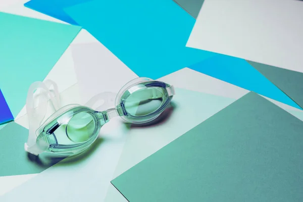 多色の幾何学的背景にラバーストラップ付きターコイズブルーのスイミンググラス 製品のコンセプト — ストック写真