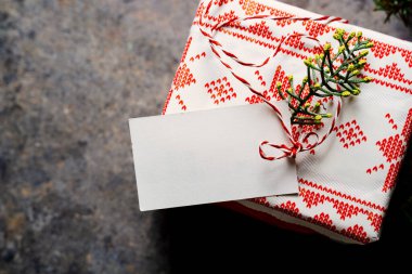 Noel hediyesi kutusu, boş etiket ve kırmızı bantla sarılı, grunge mavisi arka planda çam dallarıyla çevrili. Yukarıdan. Evde Noel konsepti