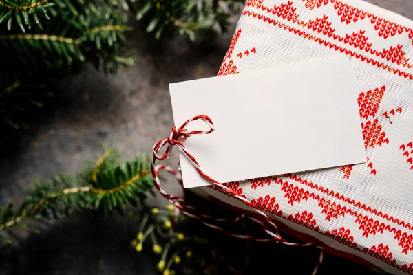 クリスマスのギフトボックスは 緑の背景に松の枝に囲まれた空のタグと赤いテープで お祝いの紙に包まれました 上から 自宅でクリスマスのコンセプト — ストック写真