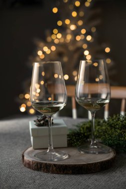 Parti hediye kutusu ve masanın üzerinde beyaz şarap kadehleri var. Odaklanmamış Noel ağacı ışıkları da var. Evde Noel