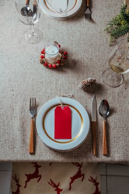 Tatil yeri dekorasyonu, boş kartlı Noel masası menüsü, süsleri ve kır bej şömine rafındaki doğal çam dalı, evde akşam yemeği. Yukarıdan gelen kuzeyli biçimi