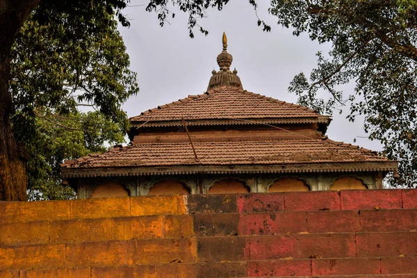 Foto en stock del antiguo pico del templo hindú, techo en forma de pirámide cubierto con azulejos hechos de arcilla y pico compuesto por metal de bronce. Templo rodeado de árboles verdes, cielo azul en el fondo en Kolhapur. —  Fotos de Stock