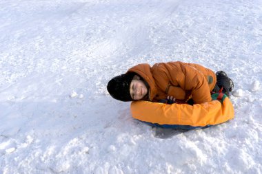 bir çocuk bir turuncu ceket ve özel bir topuz ve gülüyor kar kaydıraklı bir güneşli kış gününde siyah bir şapka.