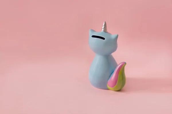 ceramic souvenir toy money box kitten Korn blue with colorful rainbow tail with unicorn horn on pink background in natural light back to camera