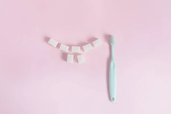 Cubes of white sugar are laid out in the form of a smile with teeth on a pink background next to the toothbrush — Stock Photo, Image