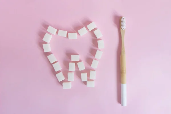 The tooth is lined with white sugar cubes on a pink background next to a bamboo toothbrush — Stock Photo, Image