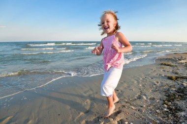 Yaz plaj üzerinde küçük güzel kız. Küçük sarışın kız plaj boyunca çalışır ve iyi eğlenceler. Yaz plaj üzerinde küçük güzel kız.