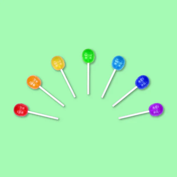 Conjunto de piruletas coloridas agrupadas en medio círculo aisladas sobre fondo verde. Caramelo en un palo. Fondo alimenticio. Puesta plana . —  Fotos de Stock