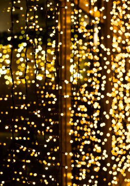 Parlayan çelenkten yapılmış Noel dekorasyonu. Yeni yıl aydınlatması. Parlak sarı ve altın parıltılı ışıklar arka plan. Defokus.