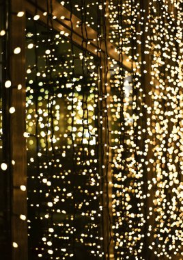 Parlayan çelenkten yapılmış Noel dekorasyonu. Yeni yıl aydınlatması. Parlak sarı ve altın parıltılı ışıklar arka plan. Defokus.