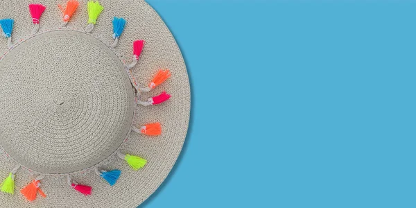 Modèle de concept d'été ou maquette. Vue de dessus sur chapeau de plage en paille avec ruban et pompons multicolores sur fond bleu. Vue du dessus . — Photo