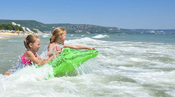 Две девушки играют на пляже на волнах. Две девушки играют надувного крокодила на волнах. Дети на пляже — стоковое фото