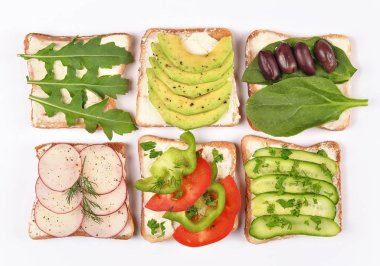 Tost ekmeği ve beyaz arka planda farklı vejetaryen malzemeleriyle hazırlanmış. Avokado, ıspanak, roka ve diğer sebzeli tost. Sağlıklı atıştırmalık ya da vejetaryen yemeği.