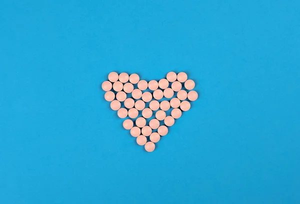 Medical background. Pink Pills in form of heart on blue background. Flat lay. — 스톡 사진