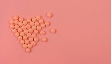 Dünya Kalp Günü konsepti. Tıbbi geçmişi var. Pembe arka planda kalp şeklinde pembe haplar..