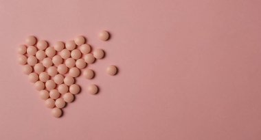 Dünya Kalp Günü konsepti. Tıbbi geçmişi var. Pembe arka planda kalp şeklinde pembe haplar..