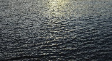 Küçük su dalgaları nehirde hareket ediyor. Doku ya da arka plan. Nehir suyunda akşam güneşi.