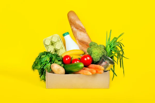 安全な食品配送または寄付の概念 コロナウイルスの隔離中の食品の配達 ヨーグルト 卵などのさまざまな食品成分を黄色の背景に入れた箱 — ストック写真