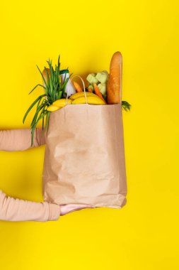 Yemek teslimatı ya da bağış konsepti. Market alışverişi. Kız ya da kadın, meyve, sebze, süt, yoğurt, sarı üzerine izole edilmiş yumurta gibi yiyeceklerle dolu bir poşet tutuyor..