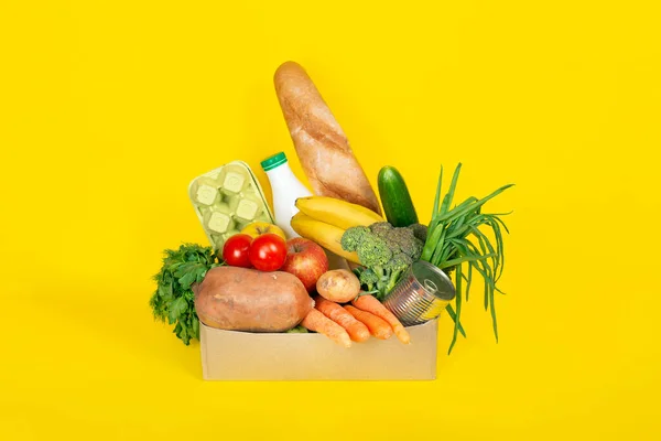 食品の配達 買い物や寄付の概念 コロナウイルスの隔離中の食品の配達 黄色の背景に単離された果物 卵などの異なる食品成分を持つ紙箱 — ストック写真