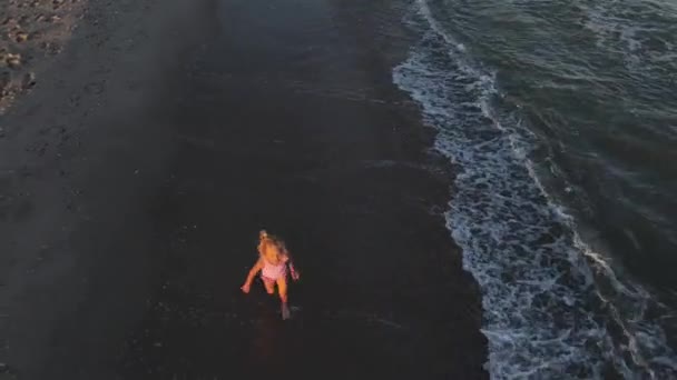 Ein kleines Mädchen im rosafarbenen Badeanzug läuft an einem einsamen Strand an der Wasserlinie entlang. Drohnenangriffe. Ansicht von oben. Kinder rennen und spielen am Strand am Meer