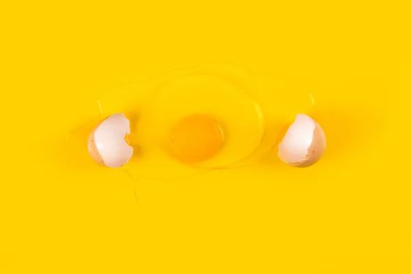 Broken raw egg isolated on yellow background. Broken egg with white shell