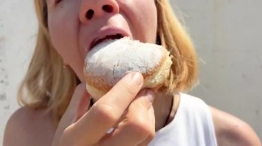 Açık havada tatlı bir donutun tadını çıkaran bir kadının yakın çekimi. Zevkle büyük bir ısırık alır. Lezzetli tatlı kavramı, hoşgörü, şeker tutkusu ve lezzetli atıştırmalık.