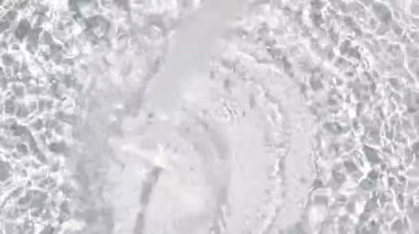 Clear water splashing on a light gray surface with sunlight reflections forming circular ripple patterns. Bright, dynamic play of light and motion captured in high detail