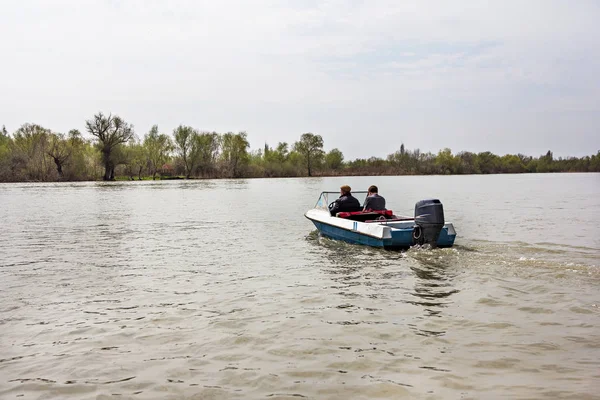 The boat sails along the river.  Two people  bottomed boat with outboard motor float along the river in the wild on a cloudy day