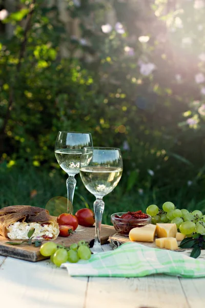Beyaz şarap ve hafif atıştırmalıklar, üzümler, şarap, peynir, turta. Doğada romantik yaz yemeği. Piknik.