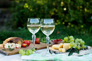 Beyaz şarap ve hafif atıştırmalıklar, üzümler, şarap, peynir, turta. Doğada romantik yaz yemeği. Piknik.