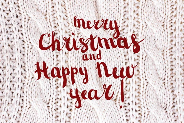 Festive Greeting Card Merry Christmas and Happy New Year with snow effect, text and White knitting wool texture background.  Knitted jersey background with a relief pattern. Braids in knitting