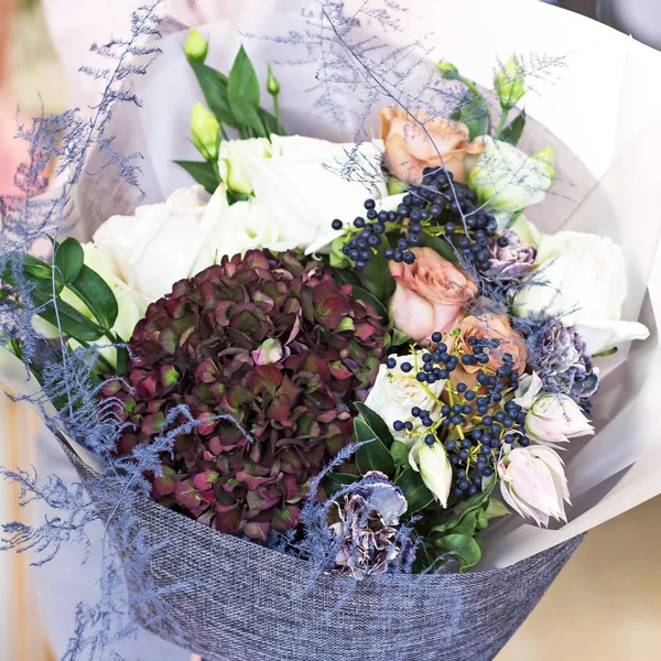 Beautiful bouquet in with roses and dark purple hydrangea. Modern, stylish bouquet in female hands