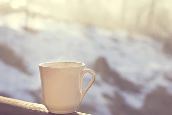 Cup with coffee, tea on the background of the winter landscape.  A cup with a hot drink on the background of the winter forest. the table outdoor in the winter. Winter time concept.