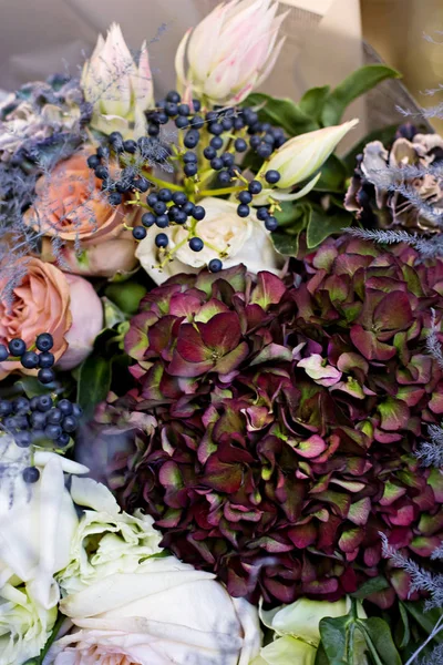 Beautiful bouquet in with roses and dark purple hydrangea. Modern, stylish bouquet in female hands